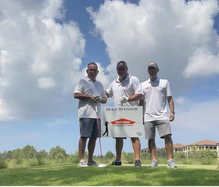 Three men posing by 'SERVPRO hole sponsor' sign on golf course