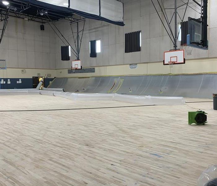 A school gym with SERVPRO equipment and plastic sheeting on the walls. 