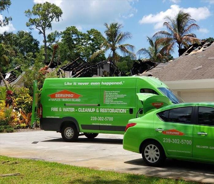 Two SERVPRO vehicles in a driveway with homes with roof damage. 