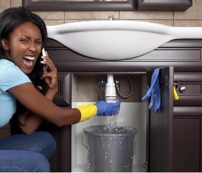 Woman on phone calling plumber after major water leak under sink
